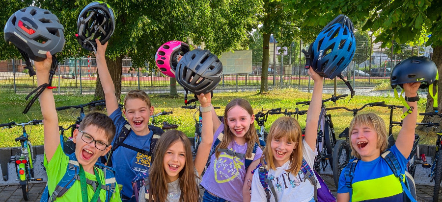 Sechs Kinder halten voller Freude ihre Fahrradhelme hoch und jubeln in die Kamera
